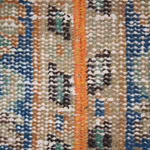 May include: Close-up of a woven rug with a repeating pattern of blue, brown, white, and orange. The rug has a fringe along the edges.