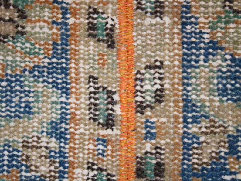 May include: Close-up of a woven rug with a repeating pattern of blue, brown, white, and orange. The rug has a fringe along the edges.