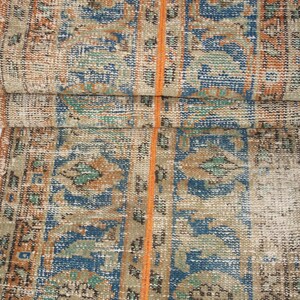 May include: A vintage rug with a faded orange, blue, and green geometric pattern. The rug has a worn and distressed look, giving it a unique character.