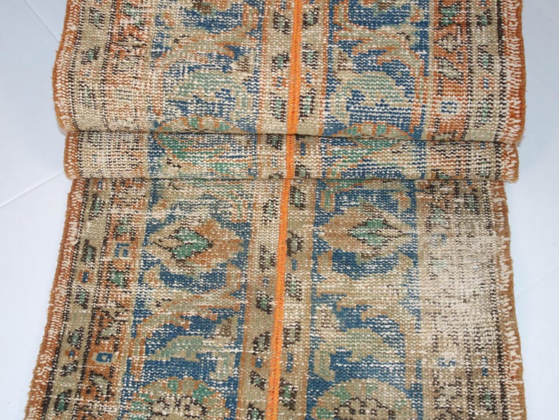 May include: A vintage rug with a faded orange, blue, and green geometric pattern. The rug has a worn and distressed look, giving it a unique character.