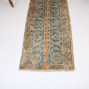 May include: A vintage runner rug with a blue, green, and orange pattern. The rug has a frayed edge and a worn look.