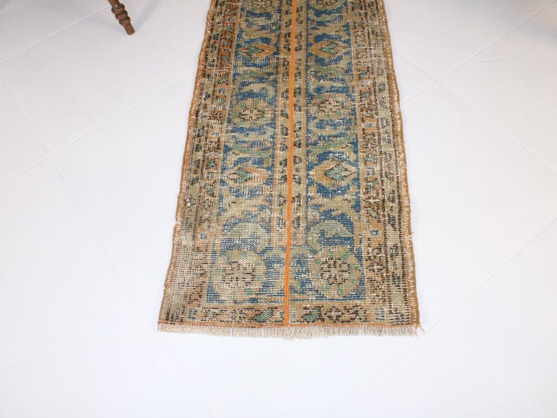 May include: A vintage runner rug with a blue, green, and orange pattern. The rug has a frayed edge and a worn look.