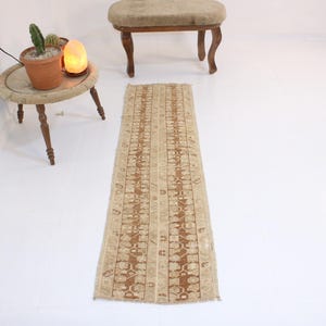 Può includere: Un tappeto da corridoio beige con un motivo geometrico marrone. Il tappeto è largo circa 76 cm e lungo 2,4 metri.