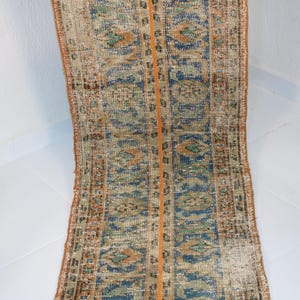 May include: A vintage runner rug with a blue, orange, and beige geometric pattern. The rug has a worn, distressed look and is perfect for adding a touch of bohemian style to your home.