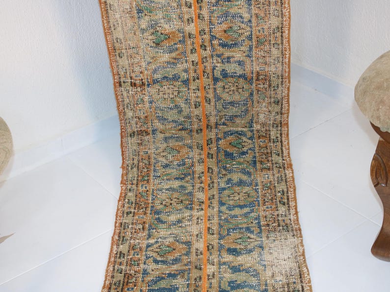 May include: A vintage runner rug with a blue, orange, and beige geometric pattern. The rug has a worn, distressed look and is perfect for adding a touch of bohemian style to your home.