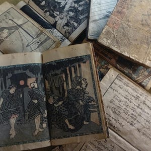 May include: A collection of antique Japanese woodblock print books. The open book displays a colorful illustration of figures in a dark setting. The covers and pages show signs of age, with faded colors and wear. The books are stacked together.