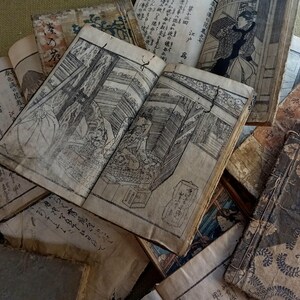May include: A collection of antique Japanese books with detailed black and white illustrations. The open book in the center displays a detailed interior scene. The aged paper and visible wear suggest the books are vintage.