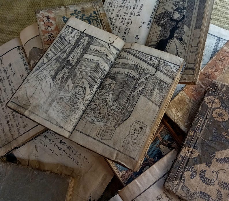 May include: A collection of antique Japanese books with detailed black and white illustrations. The open book in the center displays a detailed interior scene. The aged paper and visible wear suggest the books are vintage.