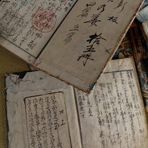 May include: An open antique book with handwritten text in black ink. The pages are aged and worn, with visible stains and markings. The book appears to be of Japanese origin, with intricate calligraphy and seals.