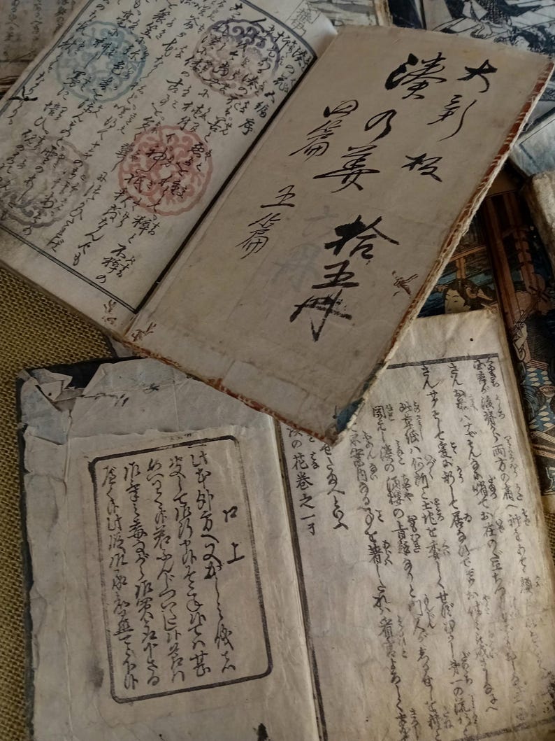 May include: An open antique book with handwritten text in black ink. The pages are aged and worn, with visible stains and markings. The book appears to be of Japanese origin, with intricate calligraphy and seals.