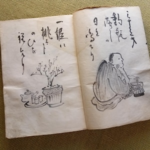 Puede incluir: Libro abierto con caligraf&iacute;a japonesa y dibujos a tinta. Una p&aacute;gina presenta una planta en maceta y un juego de t&eacute;. La otra p&aacute;gina muestra una figura sentada. Las p&aacute;ginas est&aacute;n envejecidas con un tono amarillento.