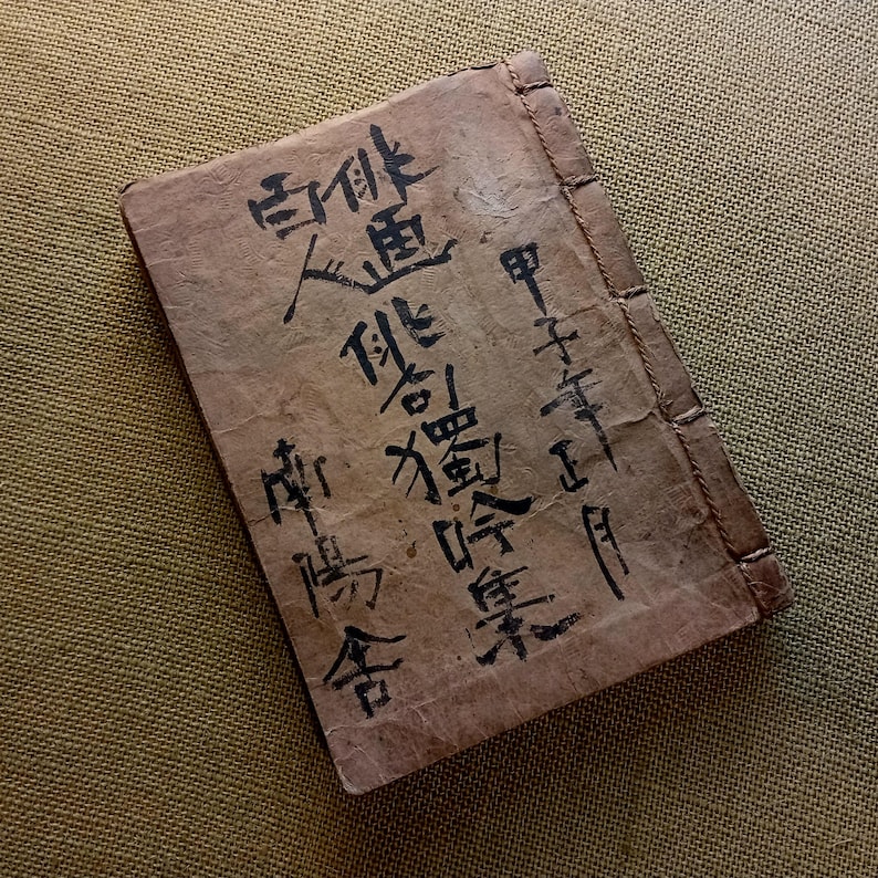 Puede incluir: Un libro rectangular vintage con una cubierta marr&oacute;n desgastada. Caligraf&iacute;a negra cubre la portada, con el t&iacute;tulo y el nombre del autor visibles. El libro est&aacute; encuadernado con un hilo visible a lo largo del lomo.