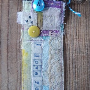 May include: A handmade fabric wall hanging with the words "I love you" in blue lettering. The hanging is decorated with various fabric scraps, buttons, and stitching.