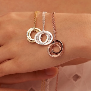 Puede incluir: Tres collares de oro, plata y oro rosa con colgantes de círculo entrelazados. Los colgantes están grabados con las palabras "I'll Love You", "Jasmine" y "July".