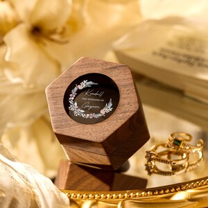 Könnte beinhalten: Eine sechseckige Holzkiste für Ringe mit einem Glasdeckel. Der Deckel zeigt ein Blumenmuster und den Text "Kendall THE WEDDING OF Grayson".