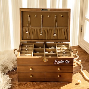 May include: A wooden jewelry box with multiple compartments and drawers. The box is open, revealing necklaces and rings. The box has a light brown finish, gold hardware, and the word "English" is written on the front.
