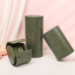 Puede incluir: Tres cajas de reloj de terciopelo verde con letras doradas. Las cajas están cerradas y colocadas sobre una superficie blanca. Una caja tiene el texto "My Jewelry", otra tiene el texto "Happy Birthday" y la tercera caja tiene un reloj dentro.