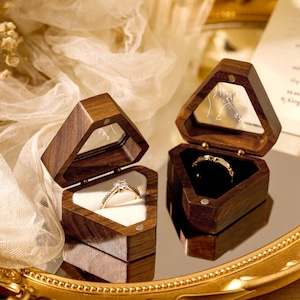 May include: Two wooden ring boxes with a diamond ring in one and a plain band in the other. The boxes are open and are sitting on a gold tray with a white fabric background.