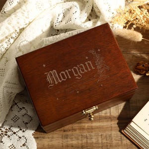 May include: A dark brown wooden box with a hinged lid and a brass latch. The box is engraved with the name "Morgan" and a floral design.