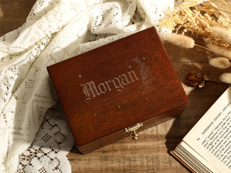 May include: A dark brown wooden box with a hinged lid and a brass latch. The box is engraved with the name "Morgan" and a floral design.