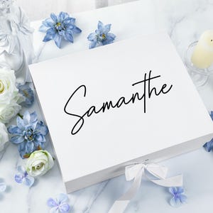 May include: White gift box with a white satin ribbon and the name "Samantha" written in black calligraphy on the top.