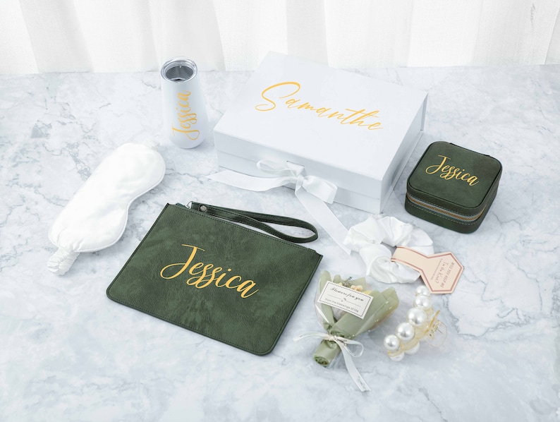May include: A green velvet pouch with the name "Jessica" embroidered in gold lettering, a white satin sleep mask, a white box with the name "Samantha" written in gold lettering, a small green velvet jewellery box with the name "Jessica" embroidered in gold lettering, a white hair scrunchie, a small bouquet of dried flowers, a pearl hair clip, and a white tumbler with the name "Jessica" written in gold lettering.