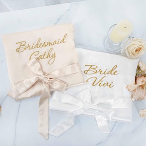Könnte beinhalten: Zwei Satin-Roben mit goldener Stickerei. Eine Robe ist weiß mit dem Text "Bride Vivi" und die andere ist beige mit dem Text "Bridesmaid Cathy".