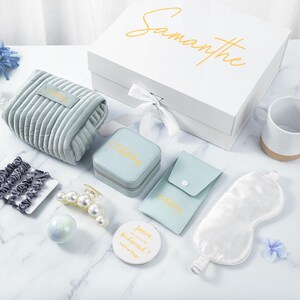 May include: A gift box with the name Samantha on the lid. The box contains a variety of items, including a blue velvet pouch, a small jewelry box, a sleep mask, a mug, hair clips, and a bath bomb. The box is perfect for a bridesmaid gift.