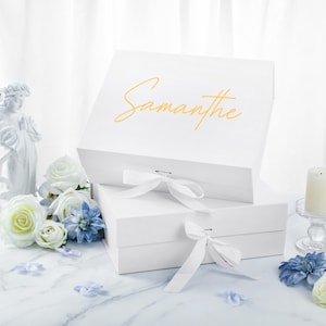 May include: White gift box with a white ribbon and the name "Samantha" written in gold lettering on the top.