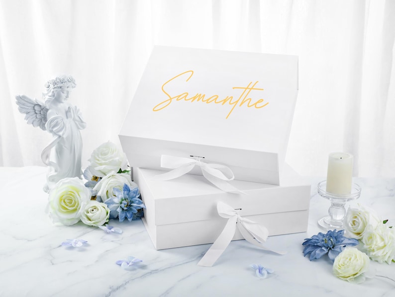 May include: White gift box with a white ribbon and the name "Samantha" written in gold lettering on the top.