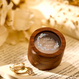 Könnte beinhalten: Eine Holzkiste für Ringe mit einem durchsichtigen Deckel und einem floralen Design. Der Deckel trägt den Text "Kendall THE WEDDING OF Gaynor".