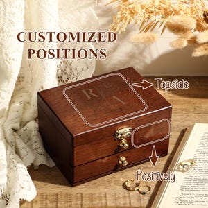 May include: A wooden jewellery box with two drawers. The top of the box has a personalised inscription with the letters "RVA". The text "Topside" and "Positively" are written on the image.