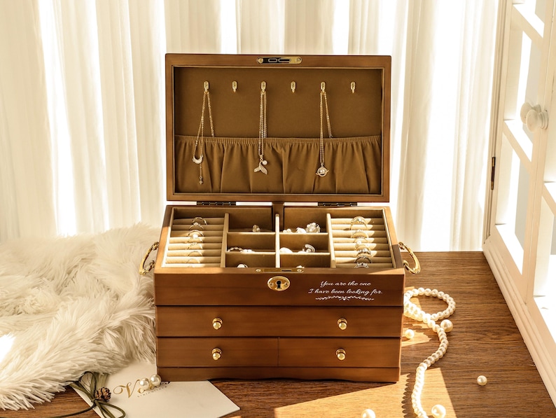 May include: A wooden jewelry box with multiple compartments and drawers, open to display necklaces and rings. The box is brown with gold hardware and a light-colored interior. The text "You are the one I have been looking for" is printed on the front.