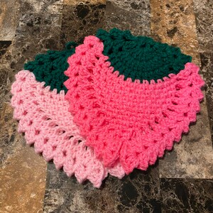 May include: A crocheted trivet in pink and green. The trivet is made of yarn and has a scalloped edge.