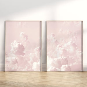 May include: Two framed prints of a pink sky with fluffy white clouds. The prints are in gold frames and are hanging on a white wall.