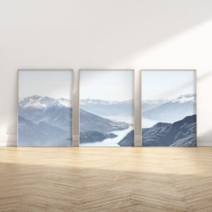 Könnte beinhalten: Drei gerahmte Landschaftsfotos einer Bergkette mit einem See im Tal. Die Fotos sind in einem hellblauen und grauen Farbschema gehalten.