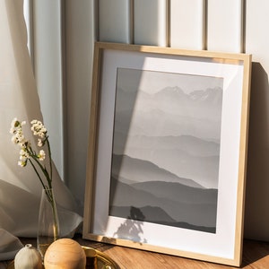 May include: A framed black and white photograph of a mountain range with a wooden frame. The photo is on a wooden floor with a gold tray, a small white vase, and a wooden ball.