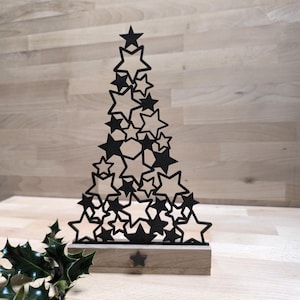 May include: Black metal Christmas tree decoration made of layered stars. The tree is standing on a wooden base.