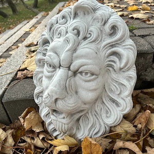 May include: A white stone lion head sculpture with detailed carvings, set against a backdrop of fallen autumn leaves.