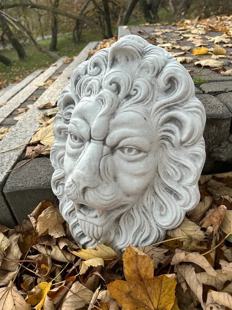 May include: A white stone lion head sculpture with detailed carvings, set against a backdrop of fallen autumn leaves.