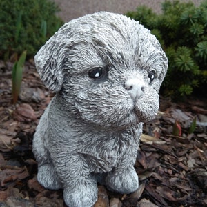 May include: A small, gray, concrete statue of a puppy sitting on a bed of wood chips.