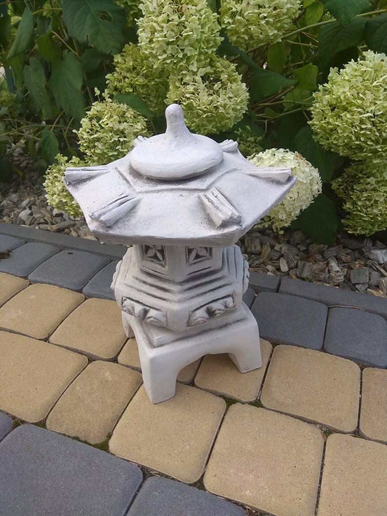 Puede incluir: Una linterna de pagodas de hormig&oacute;n blanco con un dise&ntilde;o decorativo. La linterna est&aacute; sentada en un patio de ladrillo gris y marr&oacute;n.