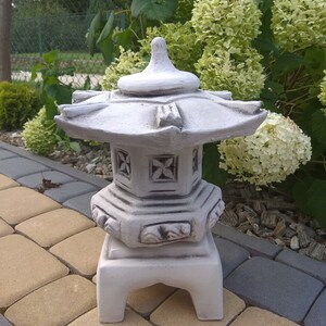 Puede incluir: Una linterna de pagoda de hormig&oacute;n blanco con un dise&ntilde;o decorativo. La linterna est&aacute; sentada en un patio de piedra.