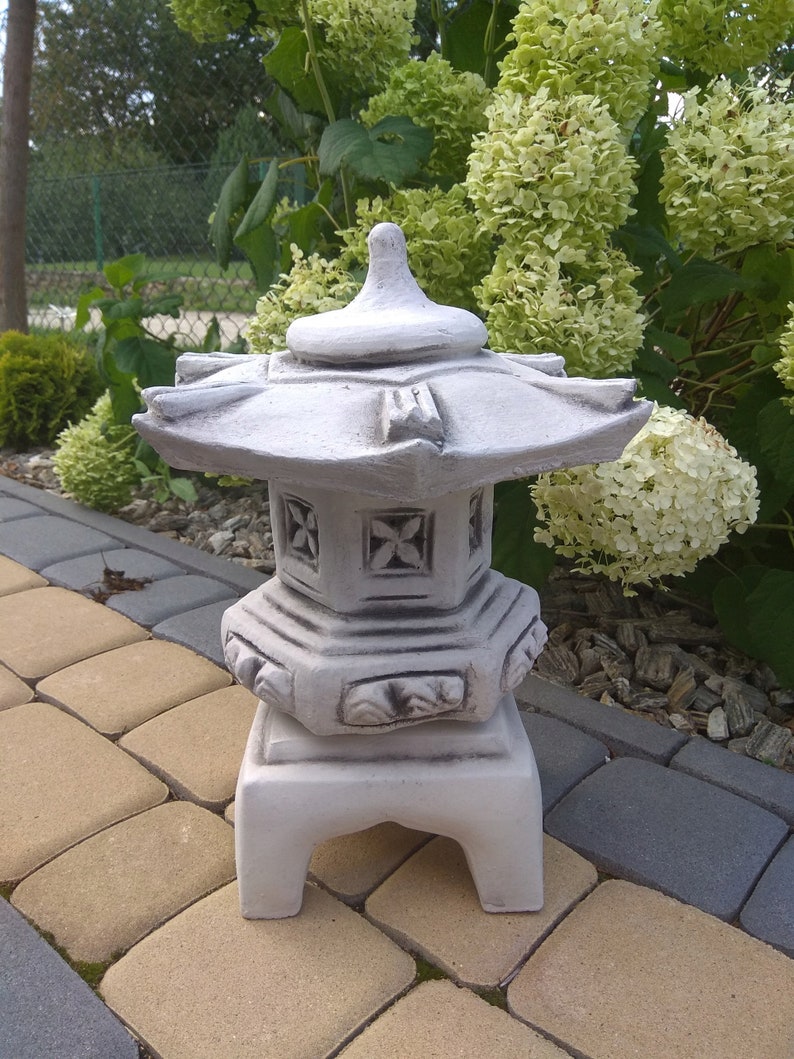 Puede incluir: Una linterna de pagoda de hormig&oacute;n blanco con un dise&ntilde;o decorativo. La linterna est&aacute; sentada en un patio de piedra.