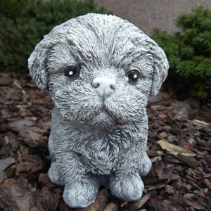 May include: A small, gray, concrete sculpture of a dog with a fluffy texture. The dog is sitting with its paws tucked underneath it and has a sweet expression on its face.