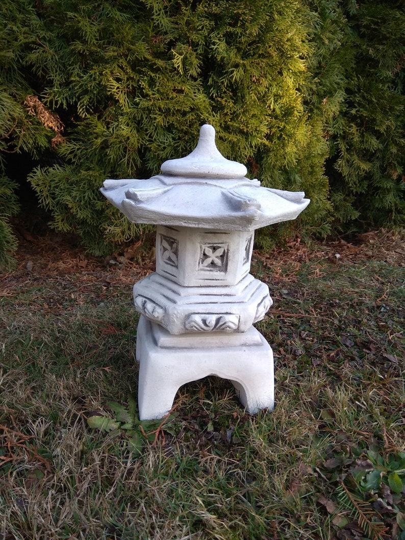 Puede incluir: Linterna de estilo pagoda japonesa de hormig&oacute;n blanco con un dise&ntilde;o decorativo. La linterna est&aacute; sentada sobre un lecho de hierba verde.