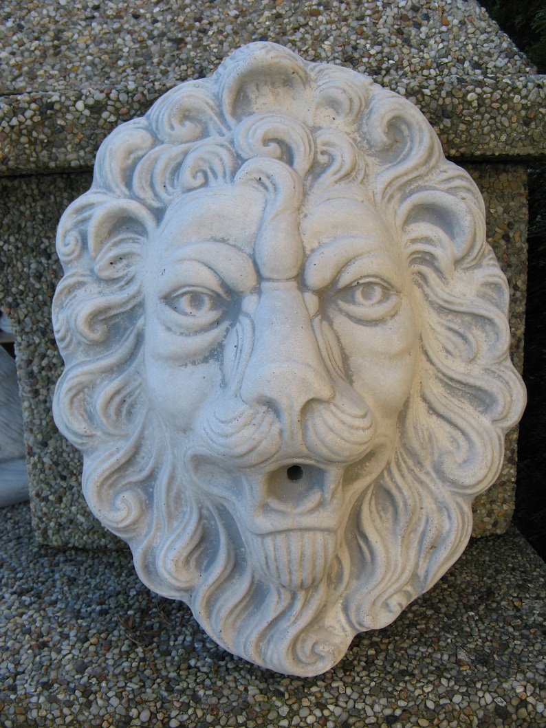 May include: A white concrete lion head sculpture with a detailed mane and a spout in the mouth. The sculpture is a garden decoration.