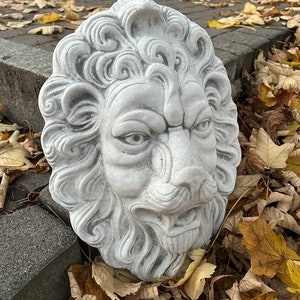 May include: A white stone lion head sculpture with detailed carvings, set against a backdrop of fallen autumn leaves.
