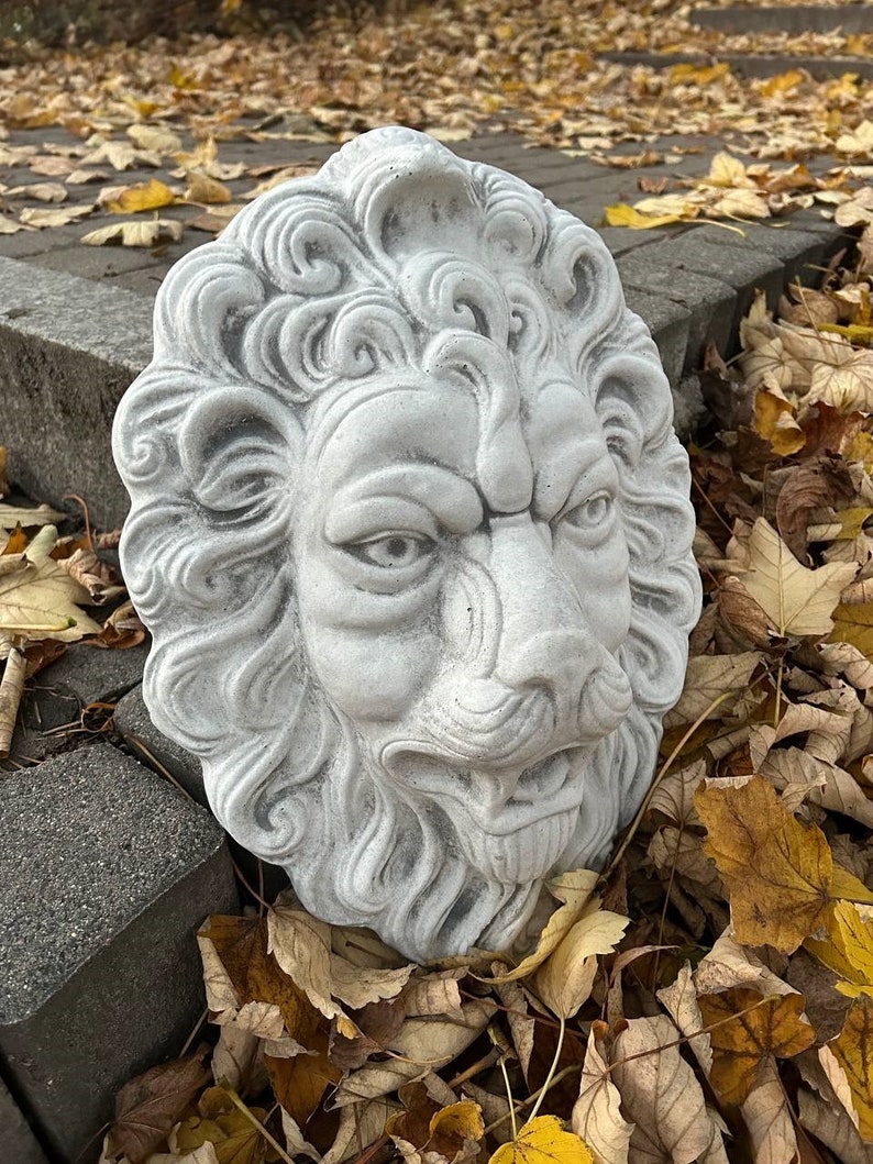 May include: A white stone lion head sculpture with detailed carvings, set against a backdrop of fallen autumn leaves.