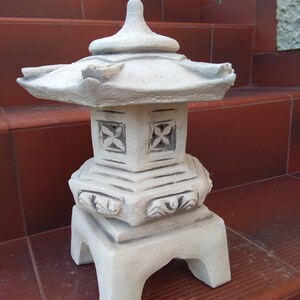 Puede incluir: Una linterna de pagoda de cer&aacute;mica blanca con detalles intrincados y una base cuadrada. La linterna tiene un techo escalonado y recortes decorativos en los lados.